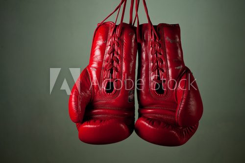 Boxing gloves hanging from laces on a grey background