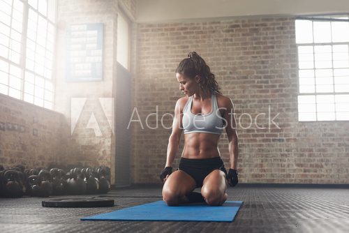 Fitness young woman sitting on yoga mat at gym