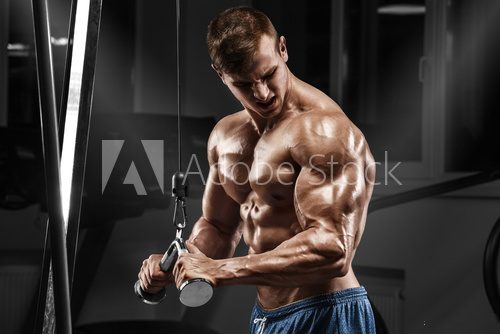 Muscular man working out in gym doing exercises at triceps, strong male naked torso abs