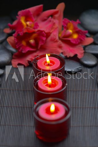 red orchid with row of candle and zen stones on mat